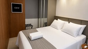 Quarto de hotel moderno com uma cama bem arrumada, mesa de cabeceira, espelho e placa indicando que o quarto está fora de serviço.