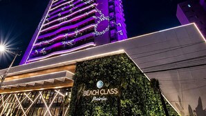 Um edifício alto com fachada iluminada por neon e uma placa com o nome 'Beach Class' hotel.