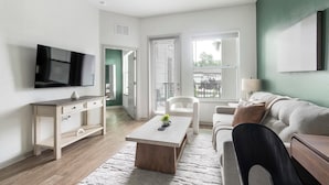 A modern living room with a flat-screen TV, a wooden coffee table, a sofa, and a chair. - Landing | Spectacular 1BD, Gym, Clubhouse (Jacksonville)