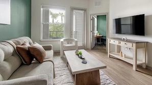 A modern living room with a sofa, coffee table, TV, and a view of the outdoors. - Landing | Stunning 1BD, Clubhouse, Gym (Jacksonville)