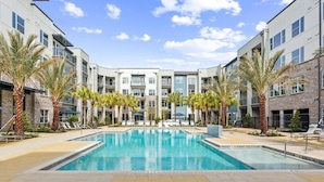 A modern building with a central pool surrounded by palm trees and lounge chairs. - Landing | Stunning 1BD, Clubhouse, Gym (Jacksonville)