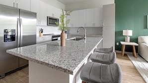 A modern kitchen with a granite countertop, stainless steel appliances, and a central island with bar stools. - Landing | Stunning 1BD, Clubhouse, Gym (Jacksonville)