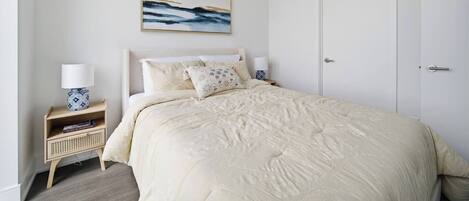 A bedroom with a bed, a nightstand, a lamp, a framed picture on the wall, and a door.
