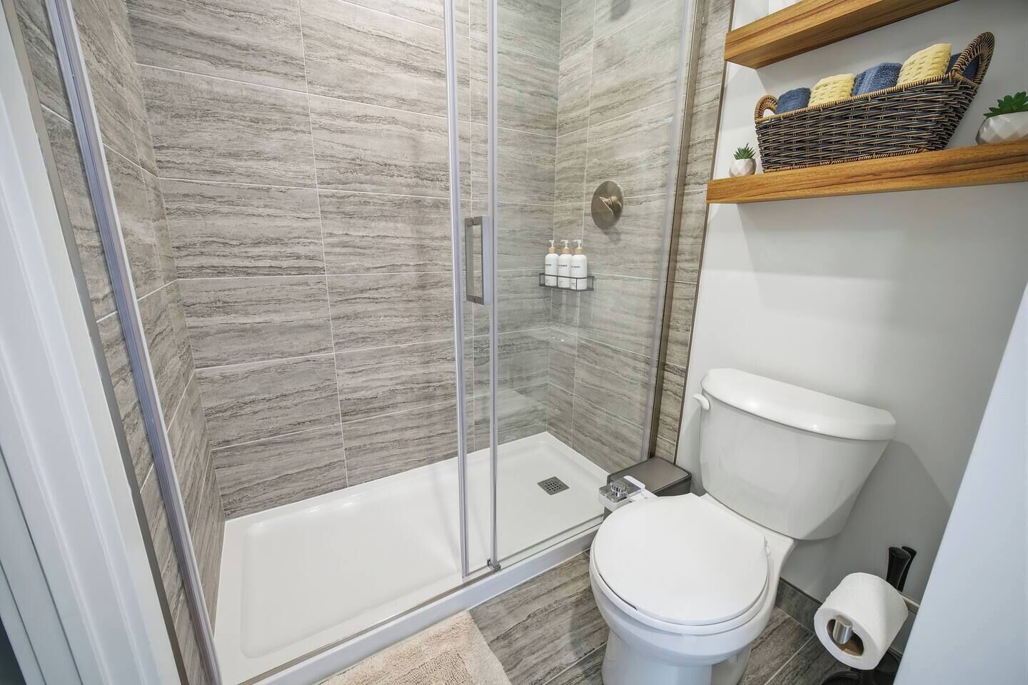 Un baño con ducha envuelta en vidrio, inodoro blanco y repisa con artículos de aseo.