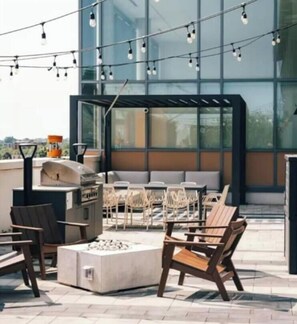 Un espace extérieur aménagé avec des chaises et un barbecue, offrant une vue sur un bâtiment moderne doté de grandes fenêtres.