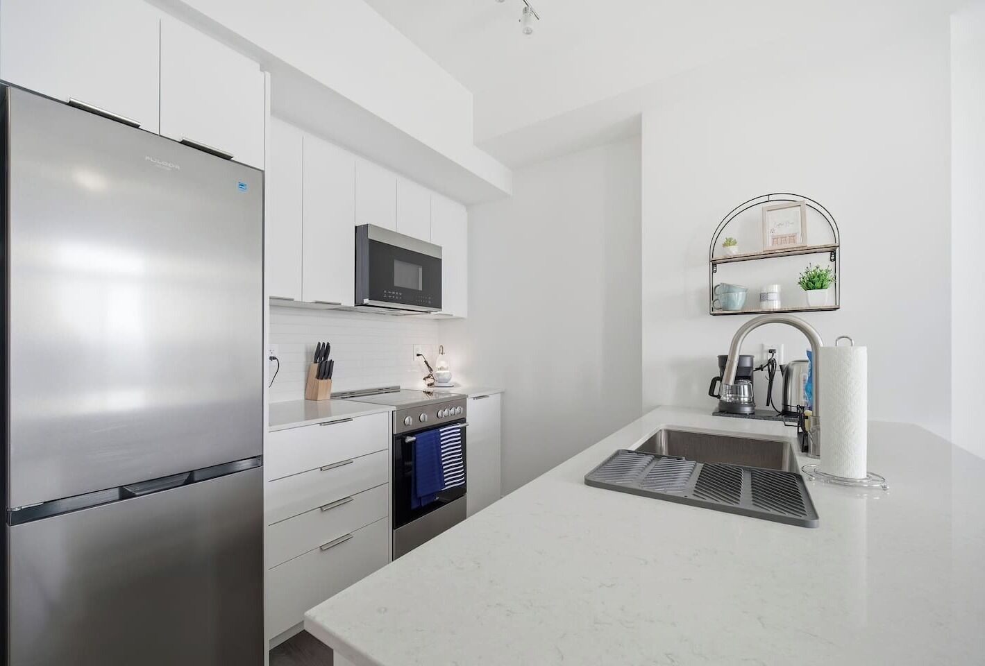 A modern kitchen with a stainless steel refrigerator, a microwave, an oven, and a sink with a towel rack.