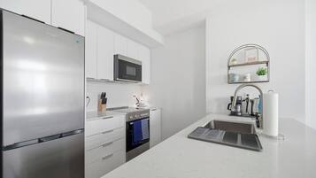 A modern kitchen with a stainless steel refrigerator, a microwave, an oven, and a sink with a towel rack.