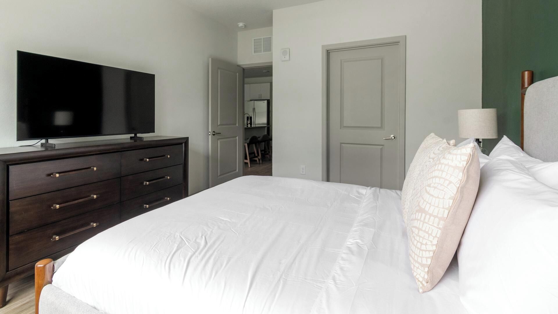 Une chambre à coucher avec un lit, une commode, un téléviseur, une porte et une lampe.