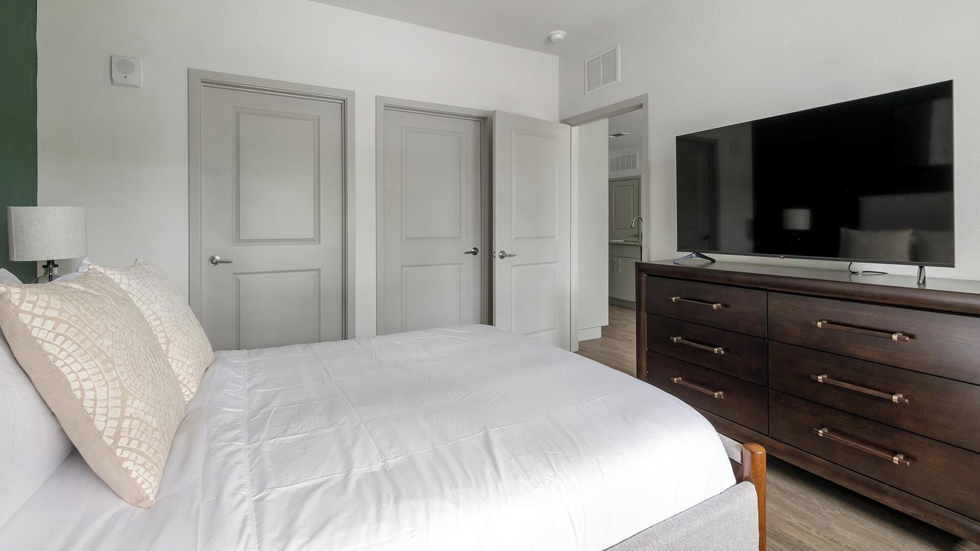 Une chambre à coucher avec un lit, une commode, un téléviseur et deux portes.
