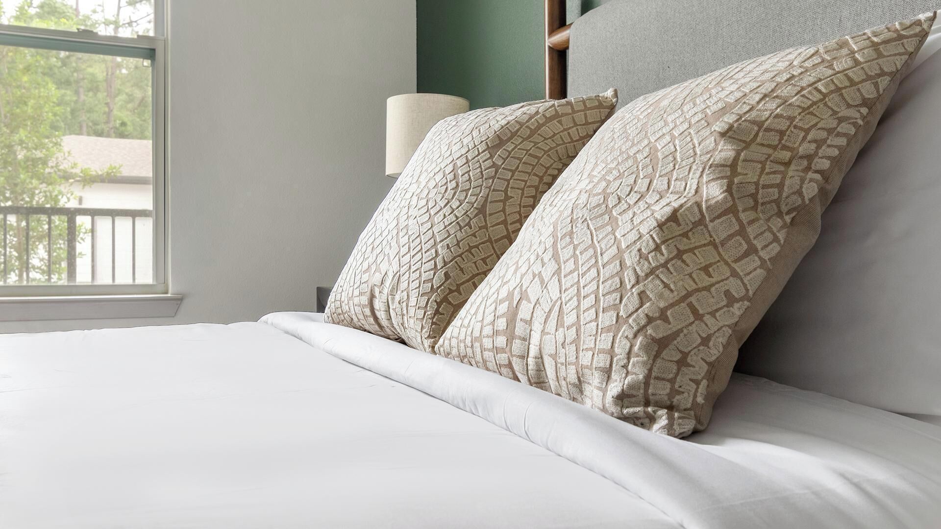 A neatly made bed with white bedding and two patterned pillows.