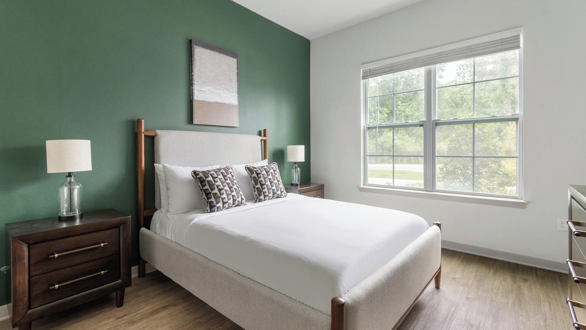 A bedroom with a bed, two bedside tables, a window, and a green wall.