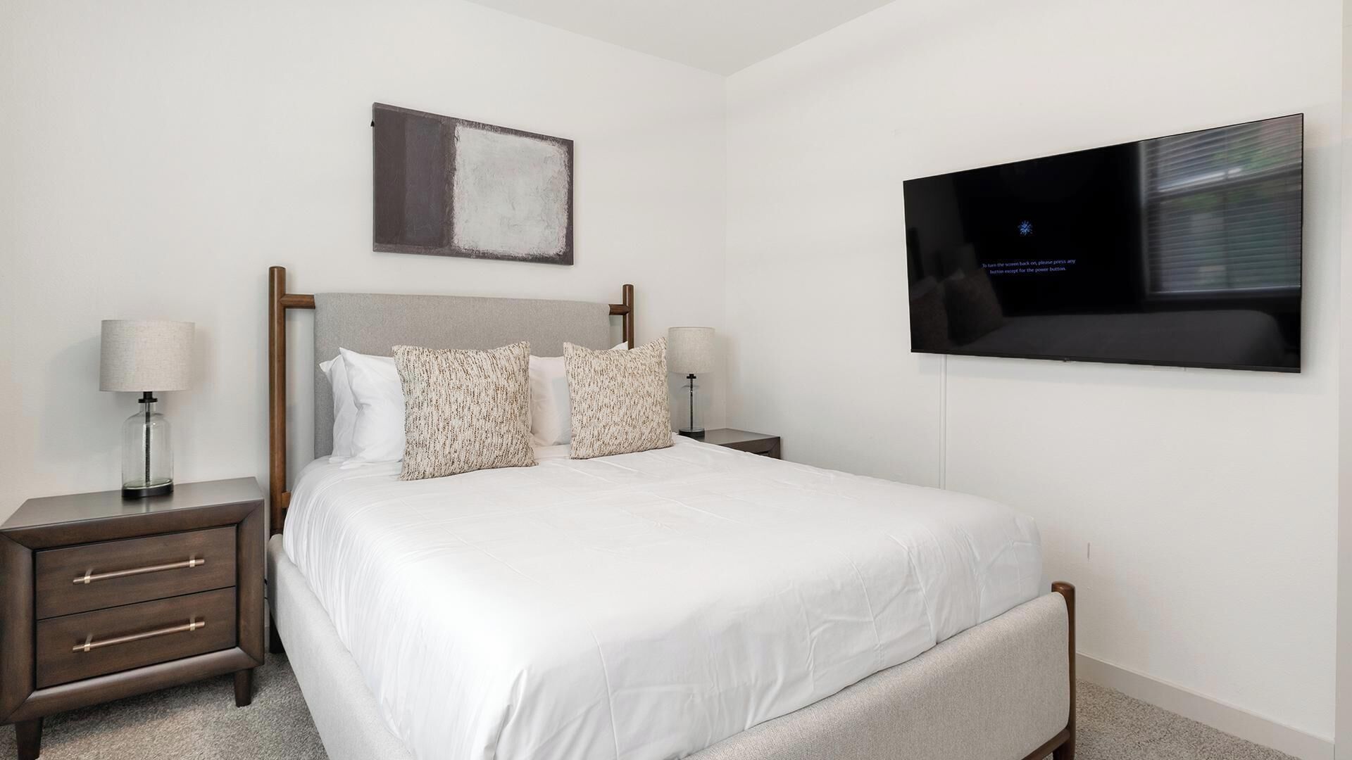 Une chambre d’hôtel avec un lit, deux tables de chevet, un téléviseur fixé au mur et un tableau au-dessus du lit.