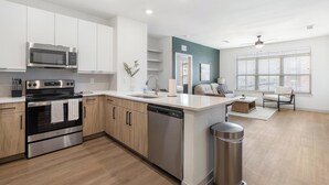 A modern kitchen with stainless steel appliances, wooden cabinets, and a dishwasher. - Landing | Stunning 2BD, Gym, Clubhouse (Celina)