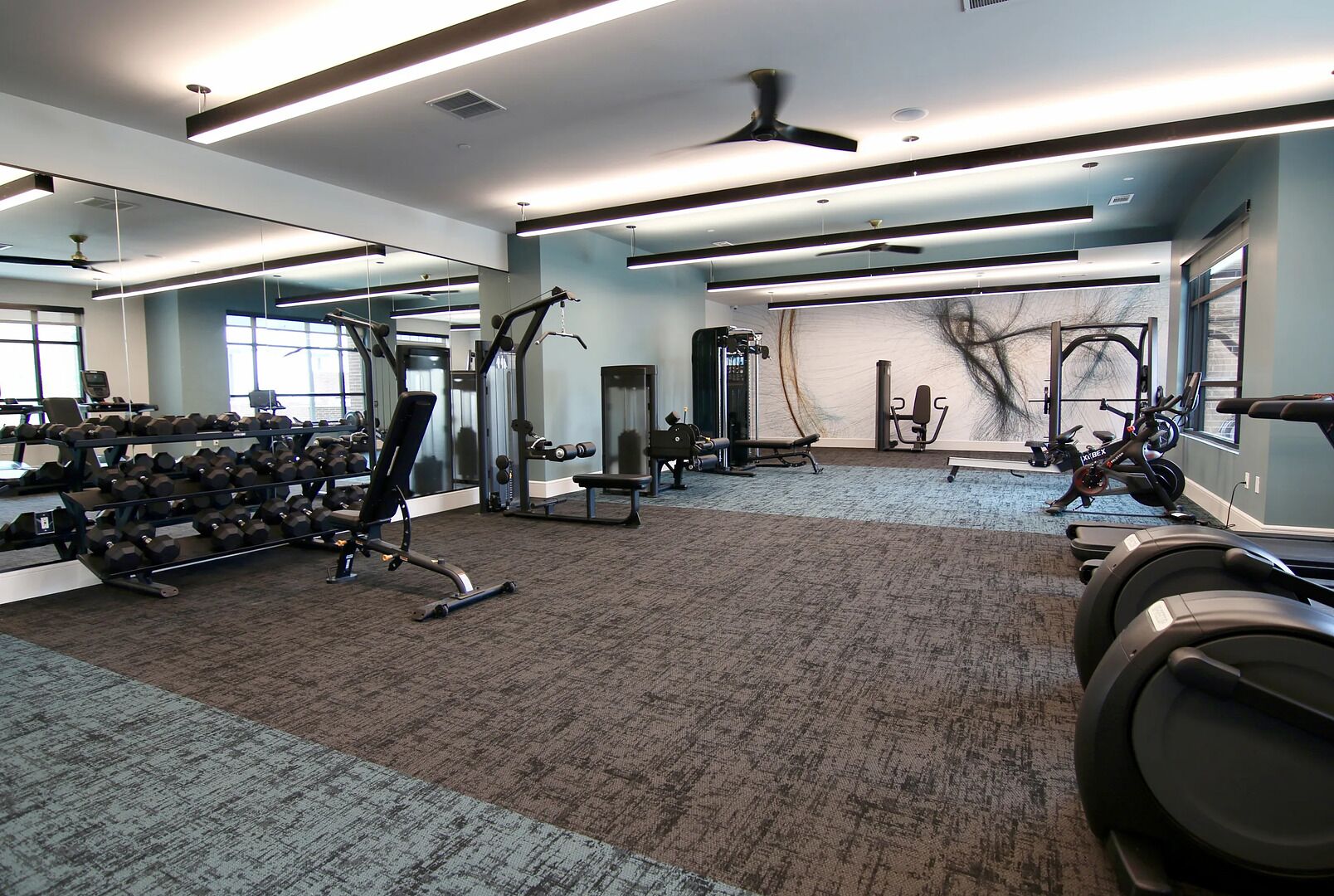 A gym with exercise equipment, mirrors, and a carpeted floor.