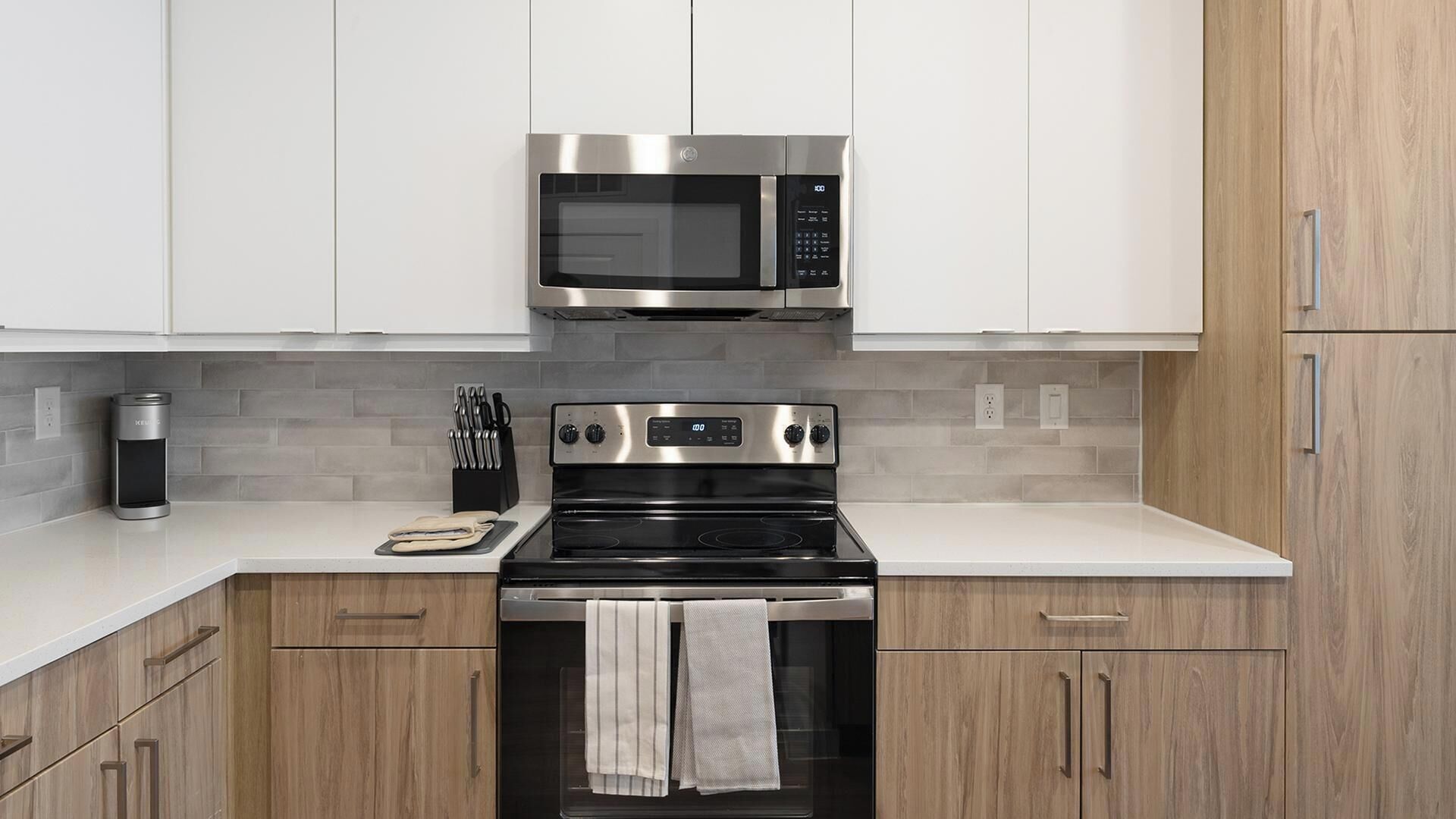 Una cocina moderna con electrodomésticos de acero inoxidable, armarios de madera y encimera blanca.