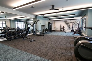 A gym with exercise equipment, mirrors, and a carpeted floor. - Landing | Chic 2BD, Courtyard, Gym (Celina)