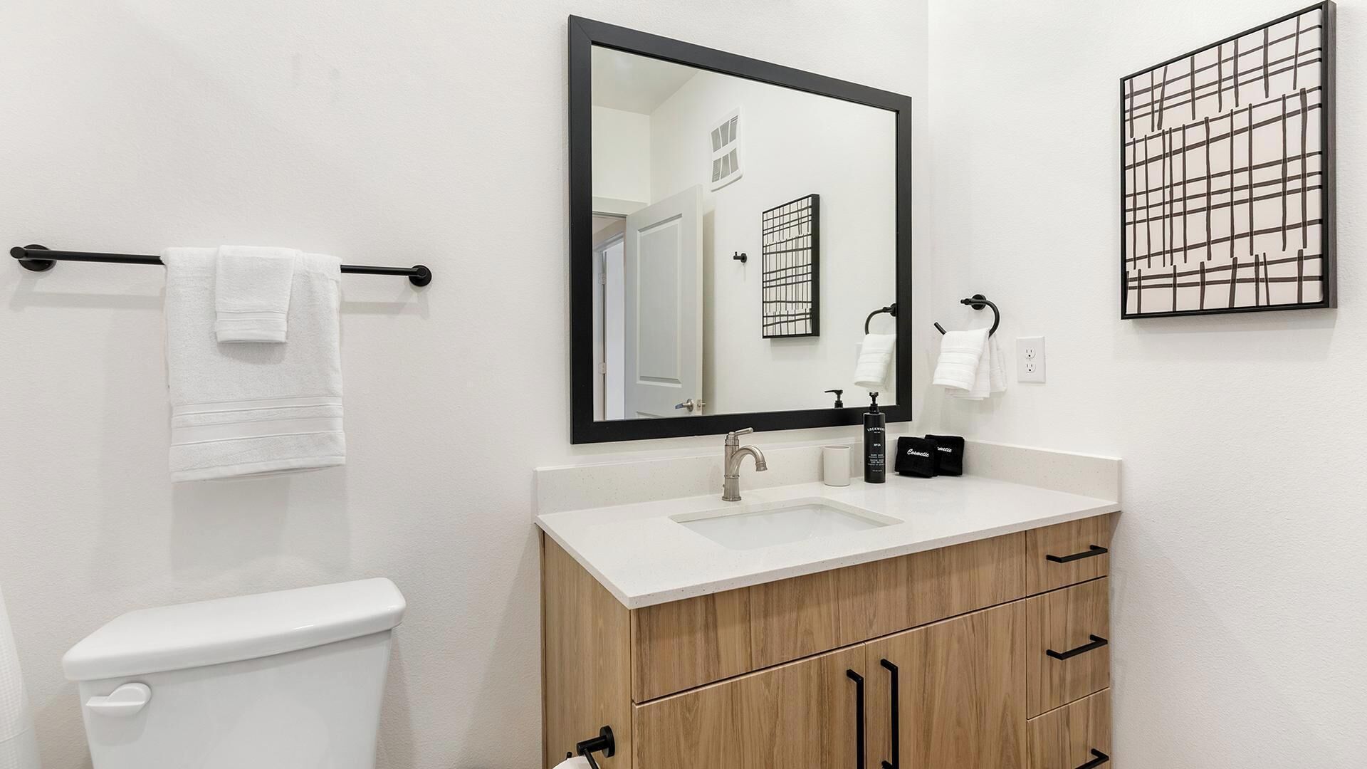 A bathroom with a white sink, a mirror, a towel rack, and wooden cabinets.