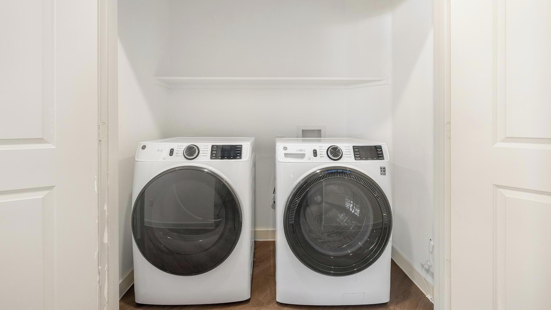 Two front-loading washing machines in a small laundry room with white walls and a wooden floor.