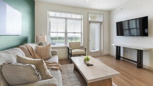 A modern living room with a sofa, armchair, coffee table, and a TV on a stand. - Landing | Amazing 1BD, Courtyard, Clubhouse (Celina)