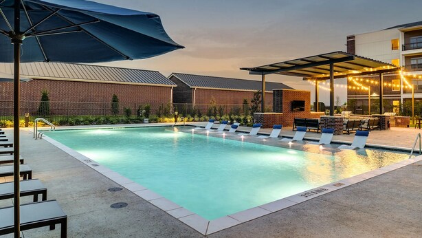 A swimming pool with lounge chairs and a barbecue area, surrounded by brick buildings and a covered patio. - Landing | Amazing 1BD, Courtyard, Clubhouse (Celina)