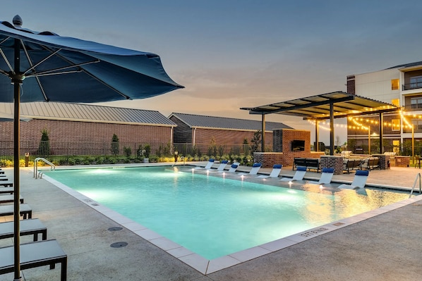 Ein Schwimmbad mit Liegestühlen und Grillplatz, umgeben von Backsteinbauten und einer überdachten Terrasse.