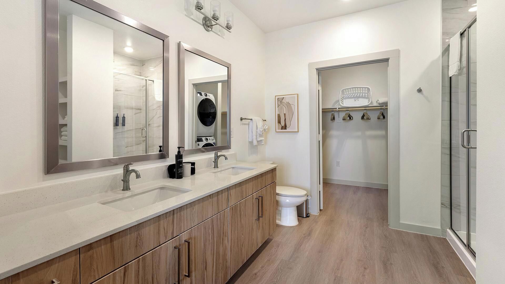 Een moderne badkamer met een wastafel met twee kommen, toilet, douche en inloopkast.