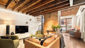 A modern living room with a TV, sofas, a staircase, and a brick wall. - 6BR Retreat, Walkers Paradise Near Washington Park (Cincinnati)