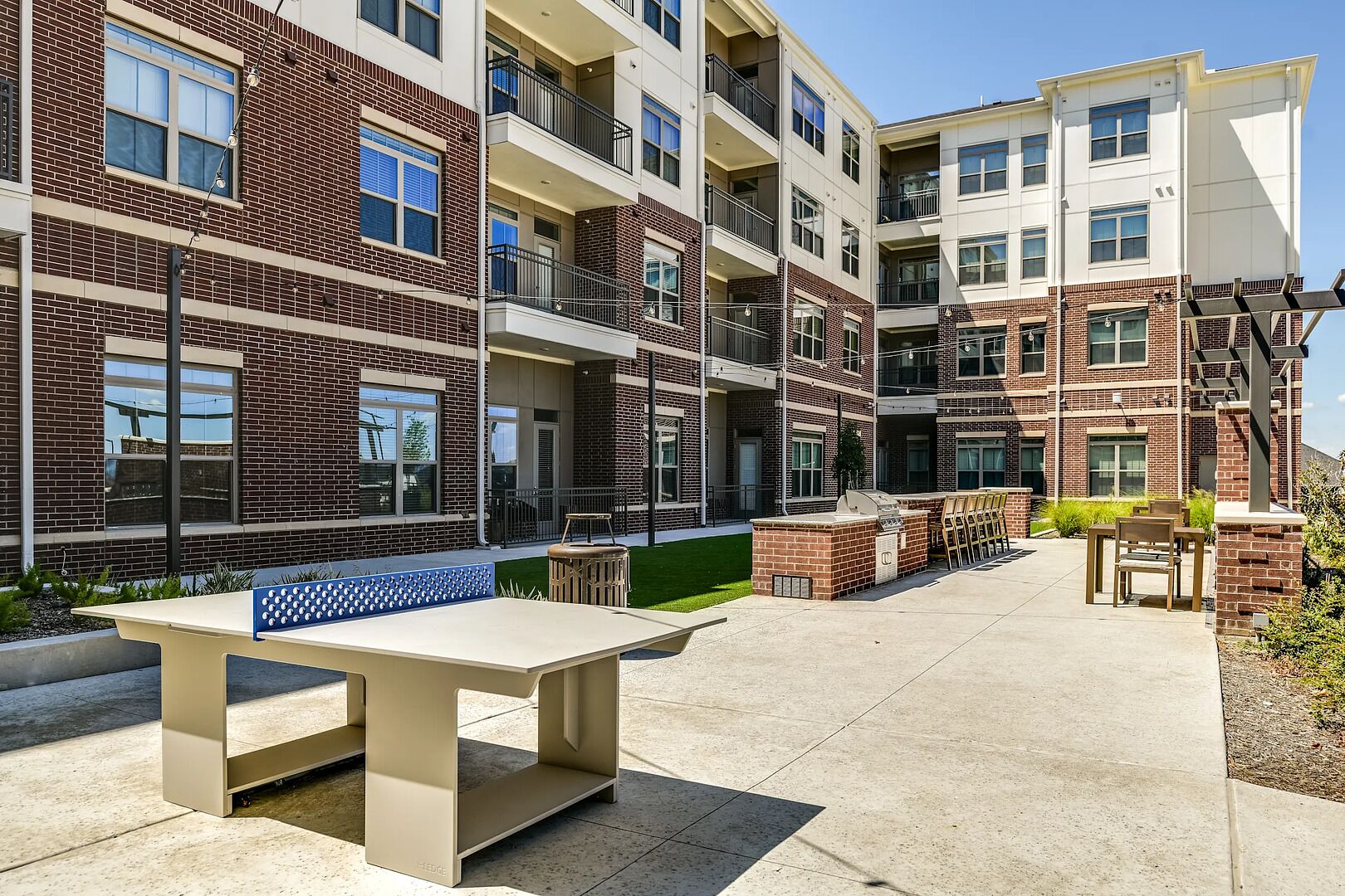 A multi-story apartment building with outdoor seating areas, a barbecue grill, and a well-maintained lawn.