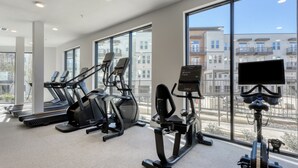 A gym with treadmills, elliptical machines, and a stationary bike, with large windows offering a view of buildings. - Landing | Incredible 1BD, Yoga Studio (San Antonio)