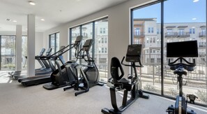 A gym with treadmills, elliptical machines, and a stationary bike, with large windows offering a view of buildings. - Landing | Incredible 1BD, Yoga Studio (San Antonio)