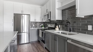 A modern kitchen with stainless steel appliances, a black tiled backsplash, and wooden flooring. - Landing | Incredible 1BD, Yoga Studio (San Antonio)