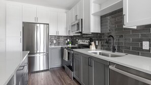 A modern kitchen with stainless steel appliances, a black tiled backsplash, and wooden flooring. - Landing | Incredible 1BD, Yoga Studio (San Antonio)
