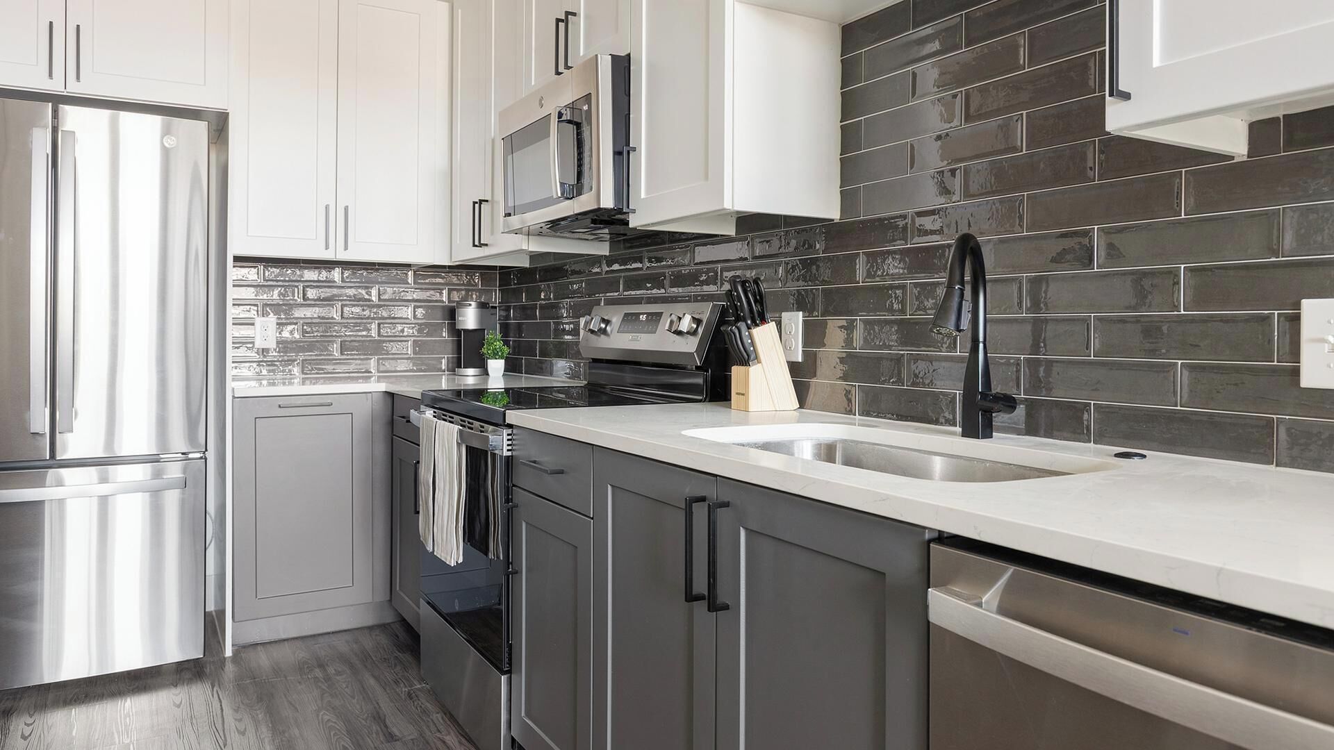 A modern kitchen with stainless steel appliances, a black tiled backsplash, and a white countertop.
