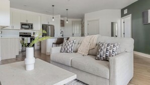 En moderne stue med sofa, sofabord og et køkken i baggrunden.