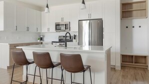 Et moderne køkken med hvide skabe, rustfrie stål hvidevarer og en central ø med barstole.