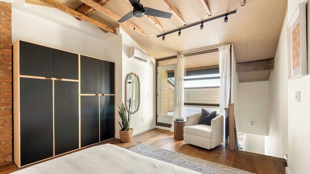 Een slaapkamer met een bed, een stoel, een spiegel, een plant en een kast.