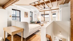 Een loft-kamer met zichtbare houten balken, een hoogslaper, een klein tafeltje en een bank.