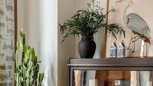 Een cactuspunt op een tafeltje, een boekenkast met diverse spullen, en een lijst met een afbeelding van een vogel aan de muur.