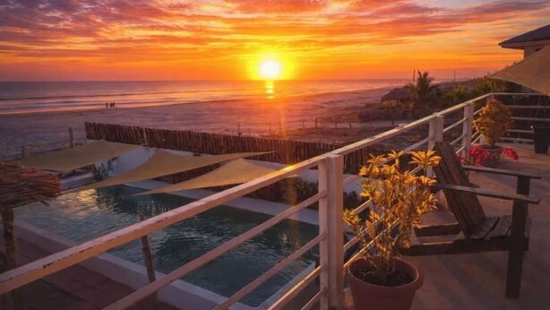Une vue sur le coucher de soleil depuis un balcon avec une piscine et un espace salon extérieur.