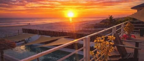 A sunset view from a balcony with a pool and outdoor seating.