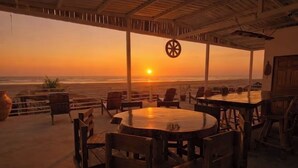 Un espace extérieur aménagé avec des tables et des chaises, offrant une vue sur l’océan au coucher du soleil.