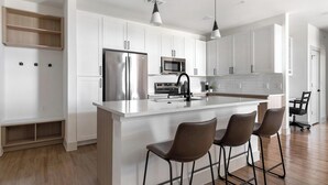 Una cocina moderna con armarios blancos, electrodomésticos de acero inoxidable y una isla central con taburetes de bar.