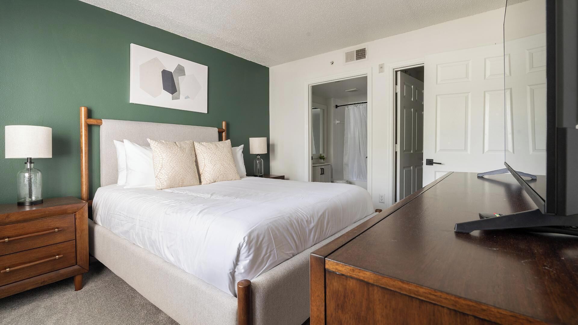 A hotel room with a bed, bedside tables, a desk, and a door leading to a bathroom.