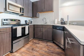 A modern kitchen with dark wood cabinets, stainless steel appliances, and a white countertop. - Landing | Spectacular 2BD, Gym, Pool (Biloxi)