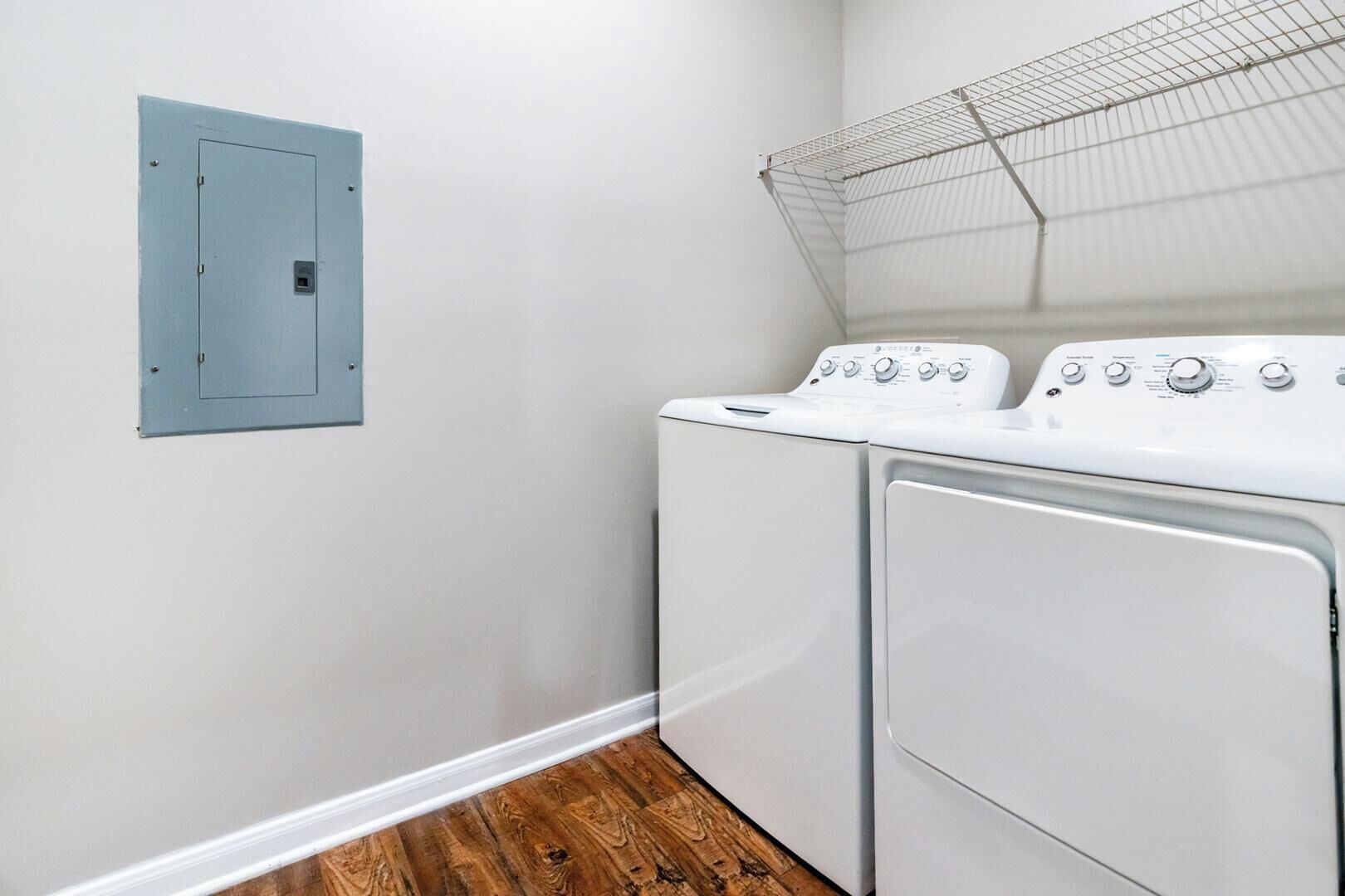 Une buanderie équipée d’un lave-linge, d’un sèche-linge et d’une boîte de raccordement électrique fixée au mur.