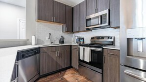 Una cocina moderna con electrodomésticos de acero inoxidable, gabinetes de madera oscura y un salpicadero de azulejos blancos.