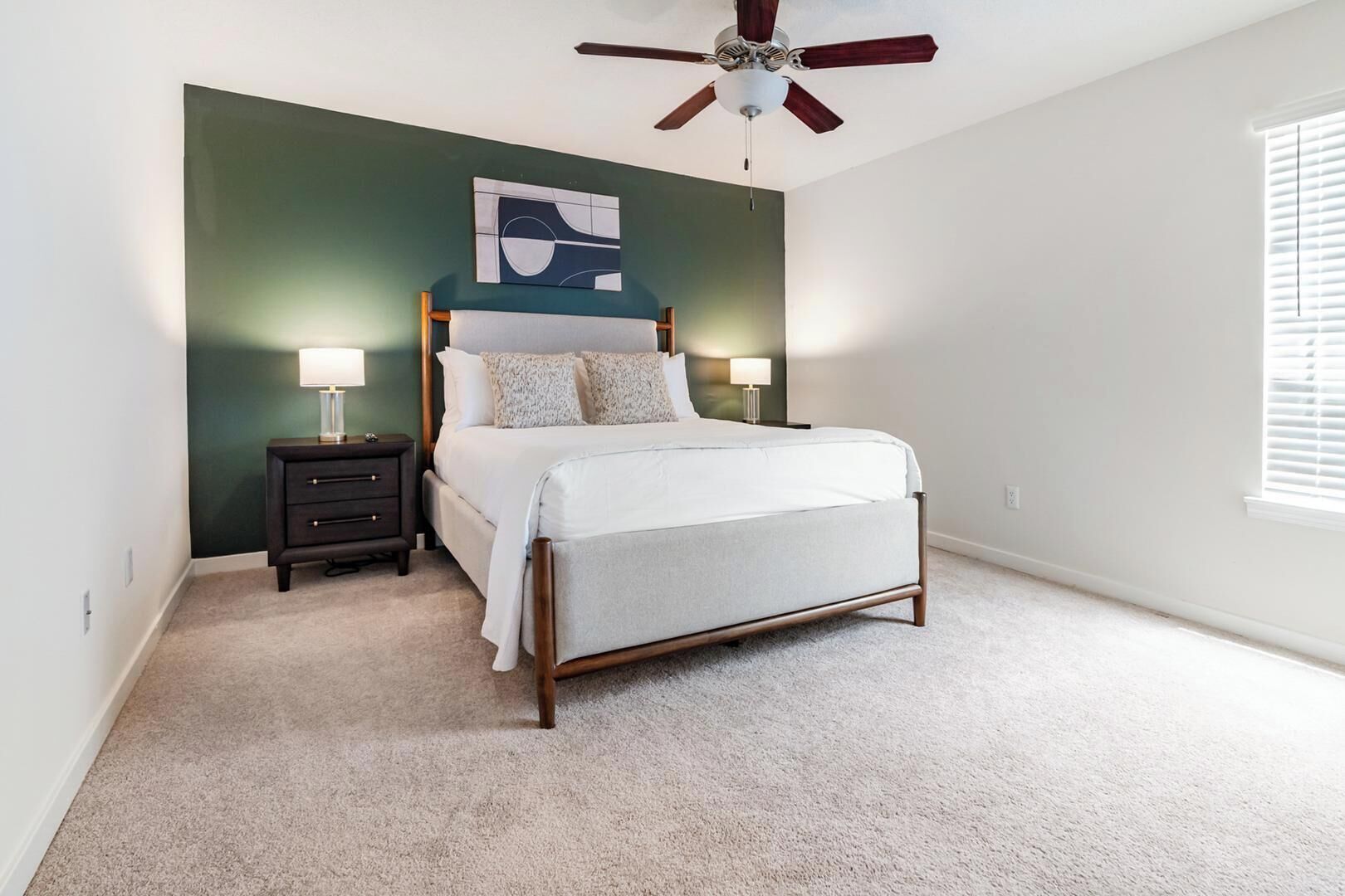 A bedroom with a bed, bedside tables, a ceiling fan, and a window with blinds.