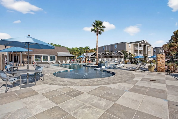 A pool area with lounge chairs, a palm tree, and a building with a blue roof. - Landing | Stylish 3BD, Game Room, Clubhouse (Gulf Hills)