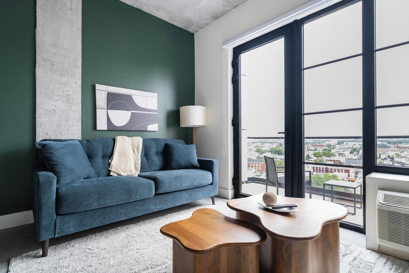 Una sala de estar moderna con un sofá azul, una mesa de centro y vistas de un paisaje urbano a través de amplios ventanales.