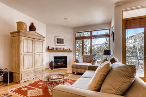 A living room with a fireplace, sofa, and large windows. - Savoy Villas 4B, Vail Top Floor 3BD Condo With Views (Vail)